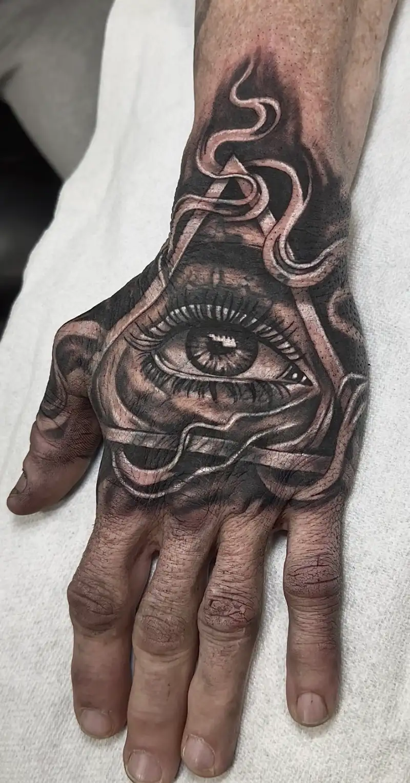 Cover up en negro y gris con un ojo central ornamental sobre la mano