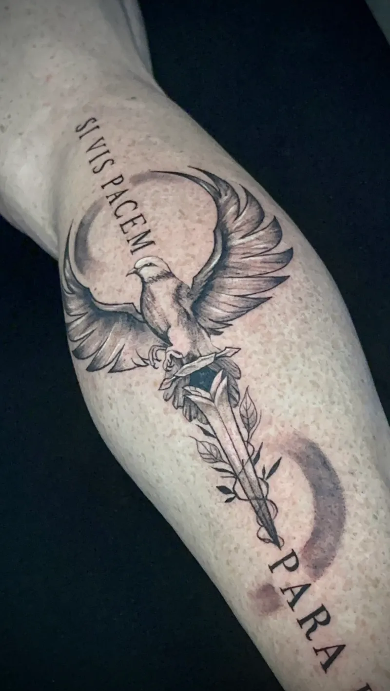Tatuaje curado en negro y gris de águila sobre espada con lema latino en el antebrazo