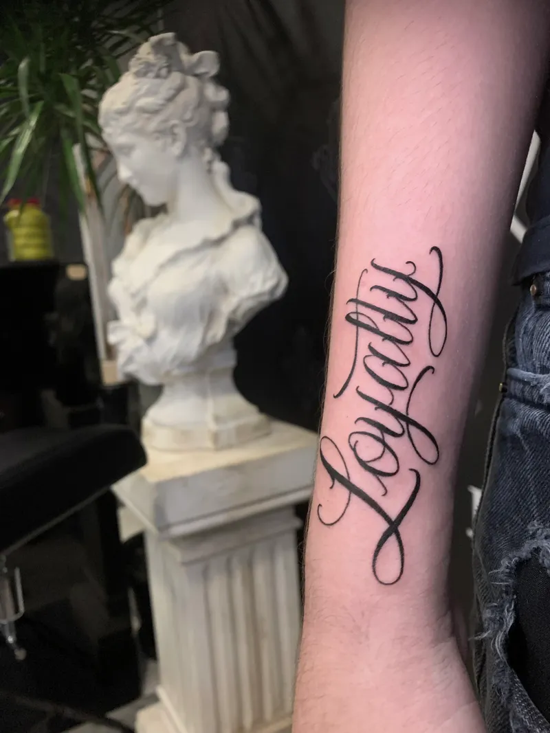 Tatuaje de lettering caligráfico Loyalty en el antebrazo