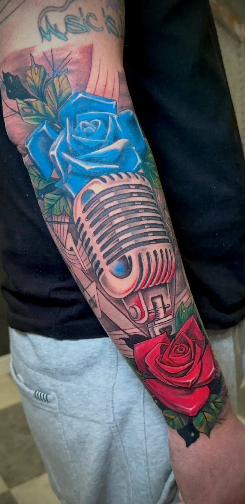 Tatuaje a color de micrófono y rosas azul y rojo en el antebrazo